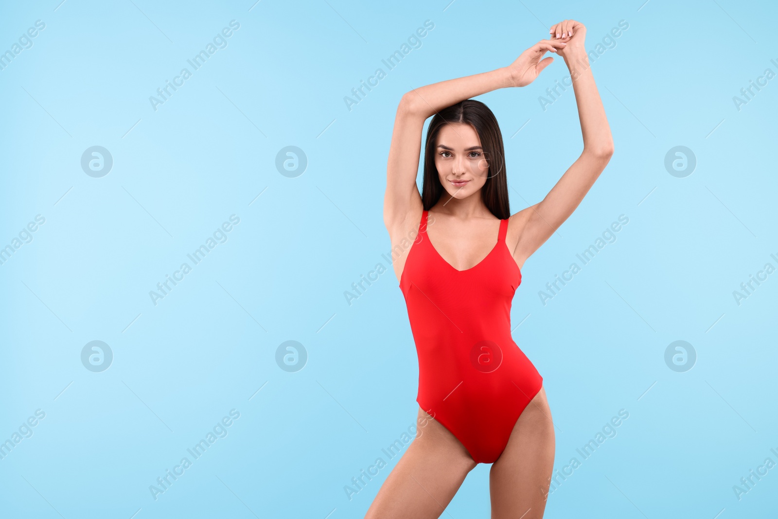 Photo of Young woman in stylish swimsuit on light blue background, space for text