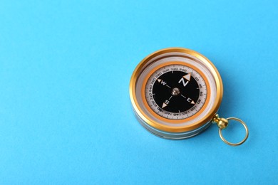 Photo of Compass on light blue background, space for text. Navigation equipment