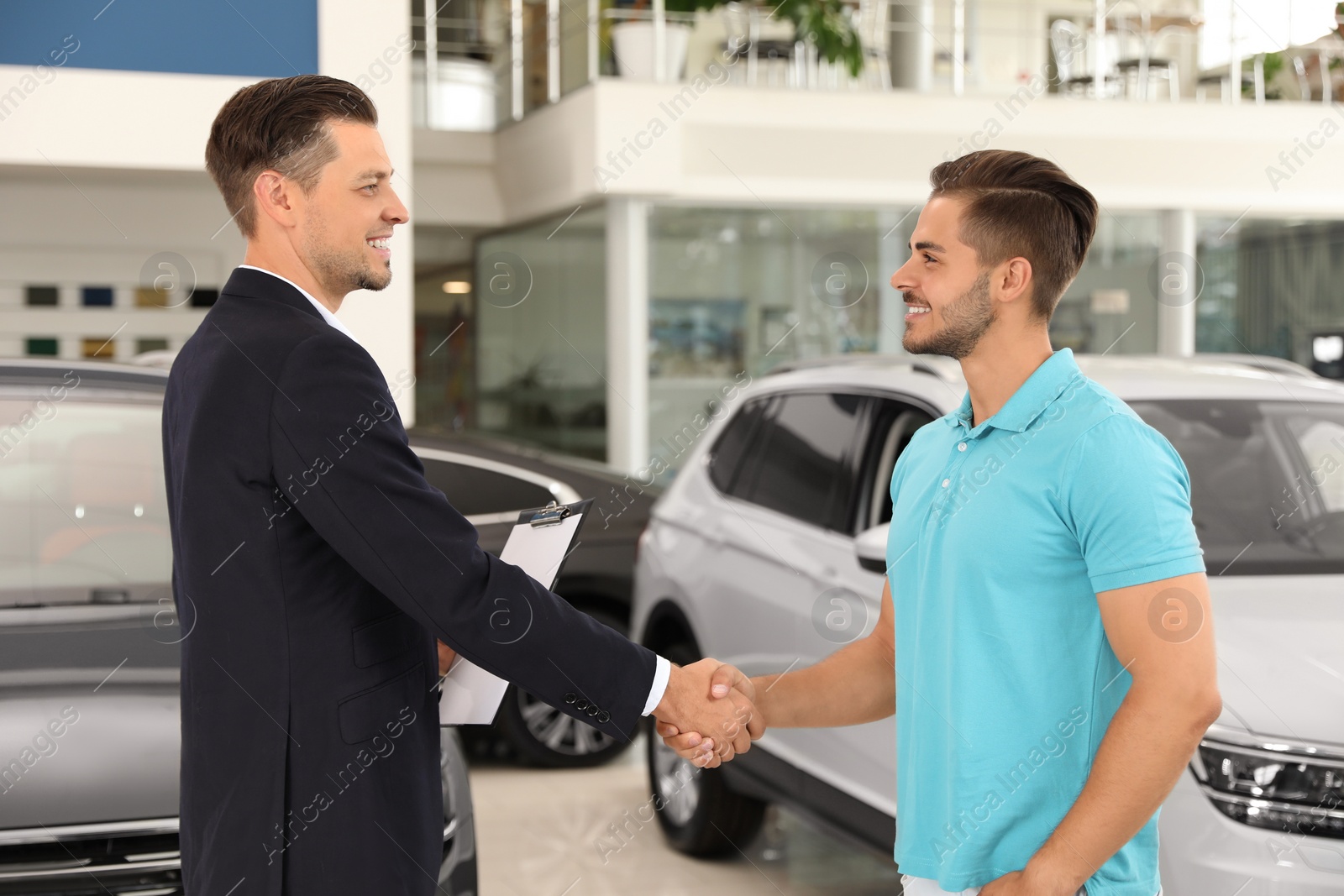 Photo of Customer and salesman shaking hands in car salon