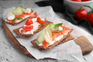 Photo of Tasty rye crispbreads with salmon, cream cheese and cucumber on wooden board, closeup