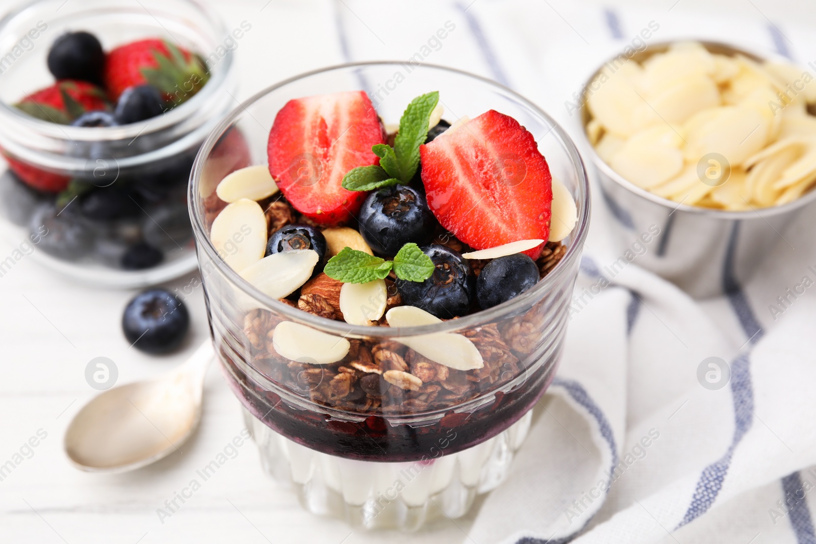 Photo of Tasty granola with berries, jam, yogurt and almond flakes in glass on white table, closeup