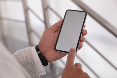 Man using mobile phone with empty screen indoors, closeup