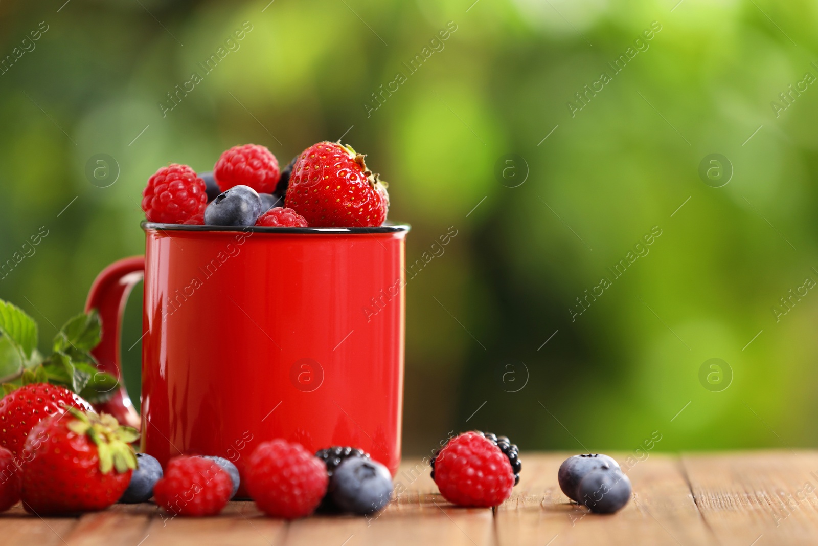 Photo of Mug with different fresh ripe berries on wooden table outdoors, space for text