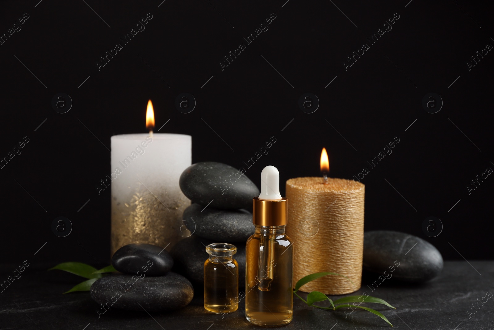 Photo of Beautiful composition with essential oil, spa stones and candles on black table