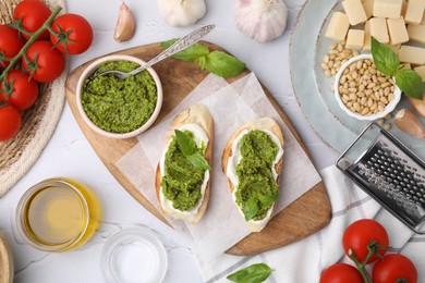 Tasty bruschettas with pesto sauce and ingredients on white textured table, flat lay