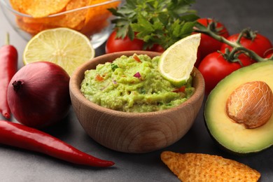 Photo of Bowl of delicious guacamole, nachos chips and ingredients on grey table, closeup