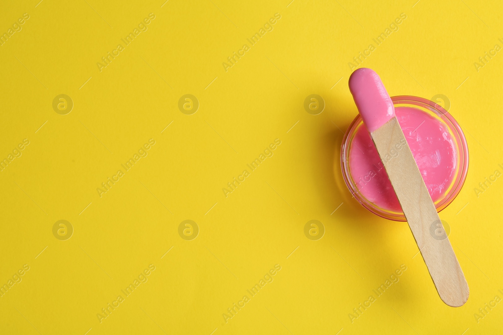 Photo of Spatula with wax on yellow background, top view. Space for text