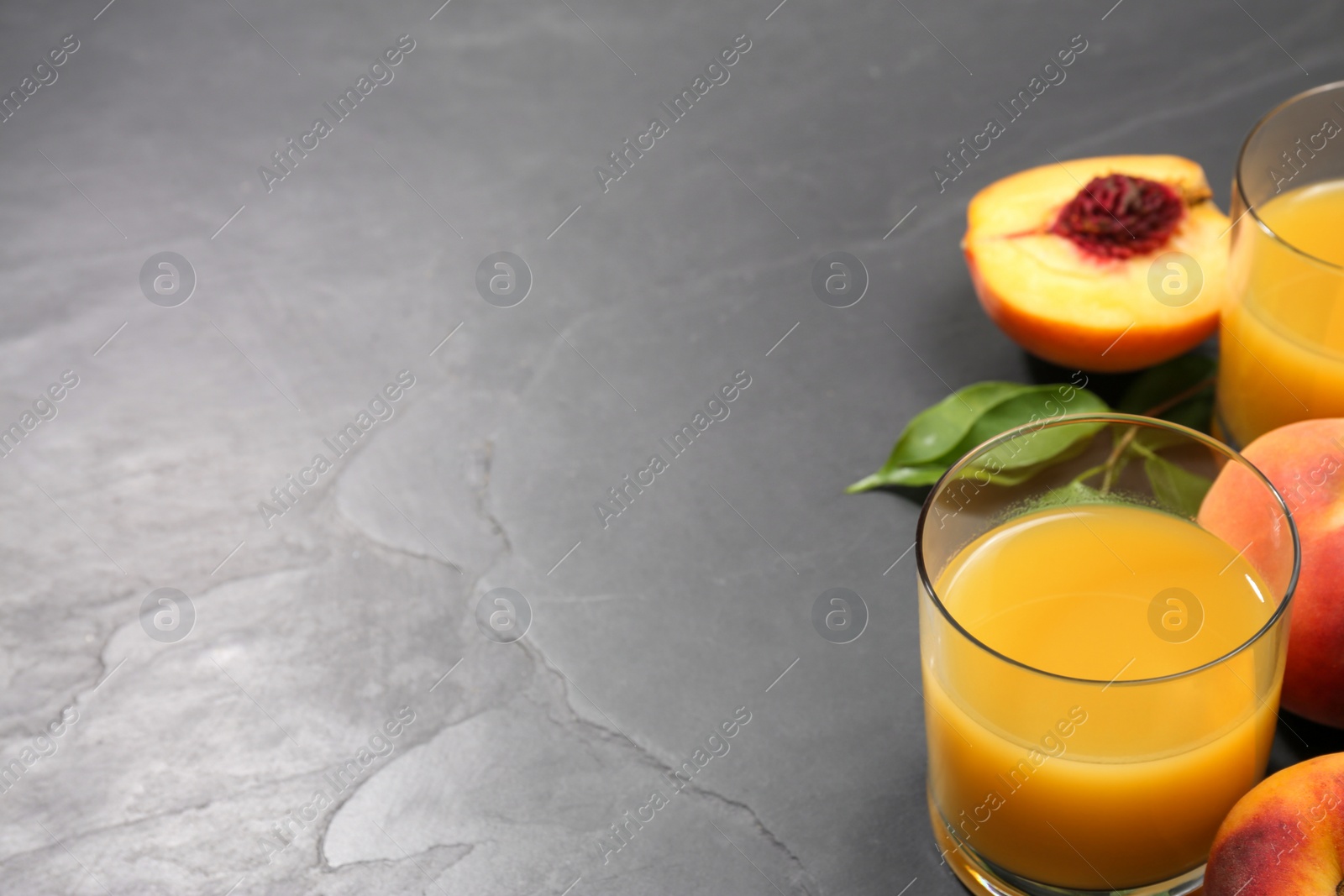 Photo of Glasses of delicious peach juice, fresh fruits and leaves on black table. Space for text
