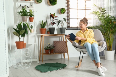 Young woman reading book in room with different home plants