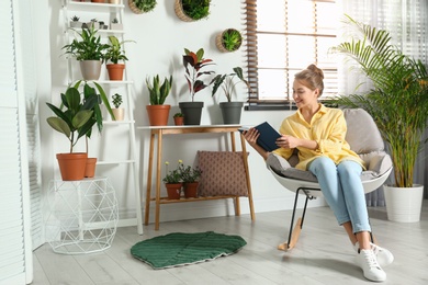 Photo of Young woman reading book in room with different home plants