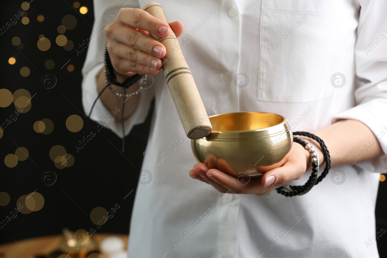 Photo of Woman using singing bowl in sound healing therapy on black background, closeup