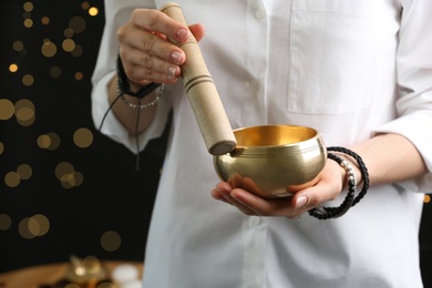 Woman using singing bowl in sound healing therapy on black background, closeup