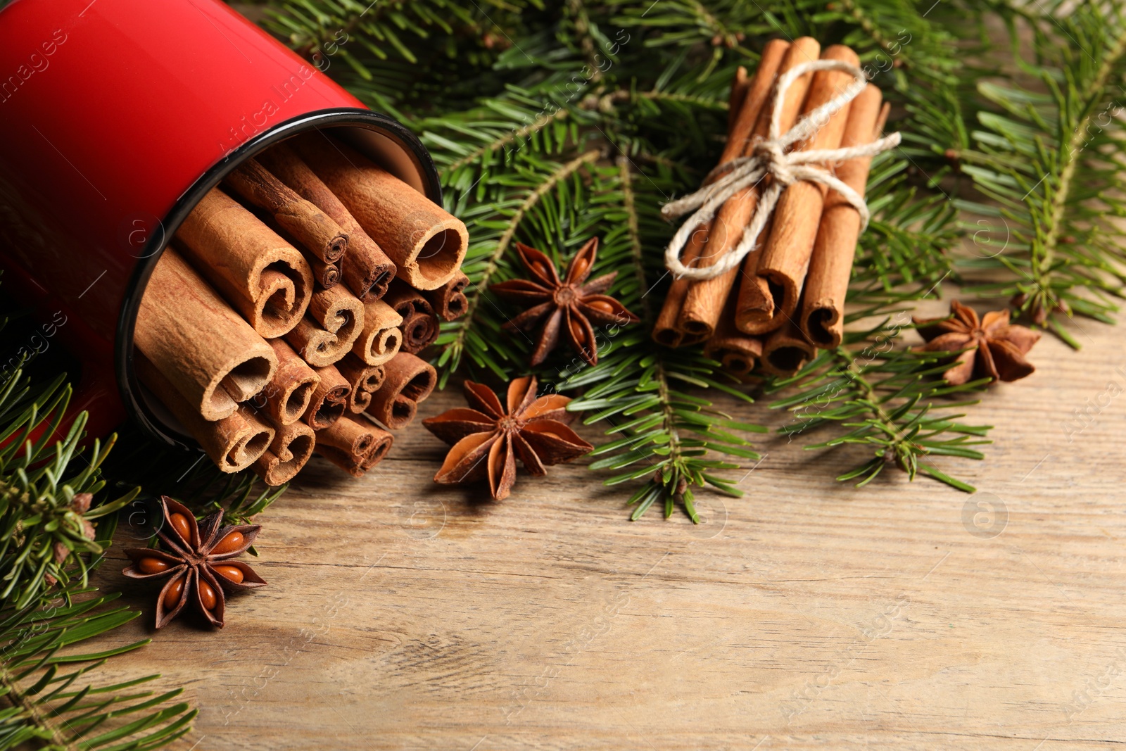 Photo of Many cinnamon sticks, anise stars and fir branches on wooden table. Space for text