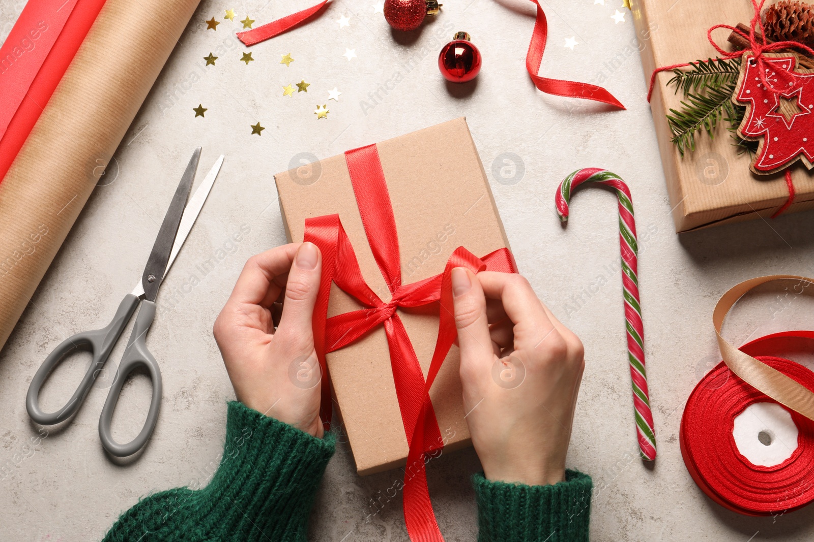 Photo of Woman decorating gift box at light grey table, top view. Christmas present