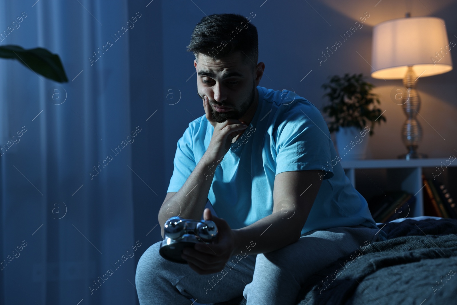 Photo of Tired man looking at alarm clock on bed