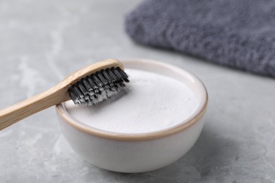 Photo of Bamboo toothbrush and bowl of baking soda on light grey table, closeup