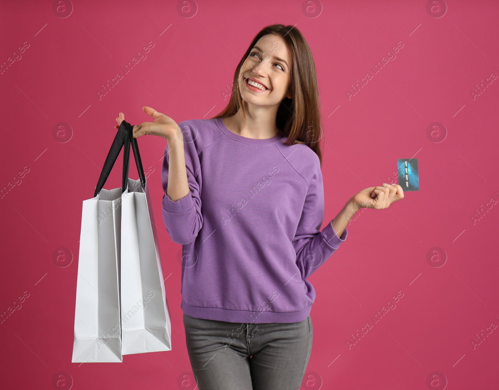 Photo of Happy young woman with credit card and shopping bags on pink background. Spending money