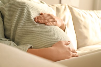 Pregnant young woman touching belly at home, closeup