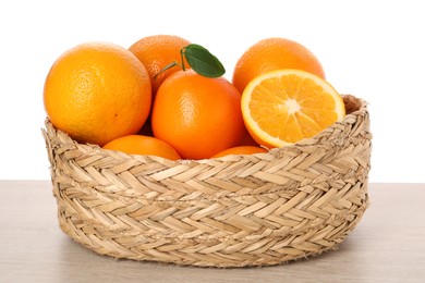 Photo of Fresh oranges in wicker basket on light wooden table against white background
