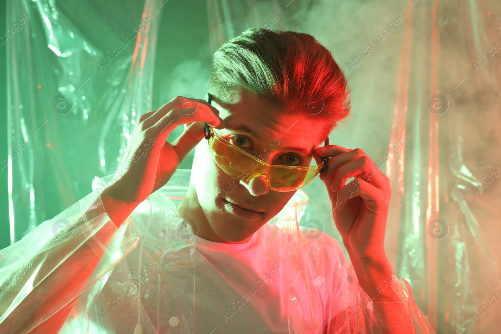 Photo of Stylish young man wearing clear coat and glasses in neon lights