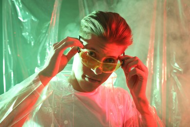 Photo of Stylish young man wearing clear coat and glasses in neon lights