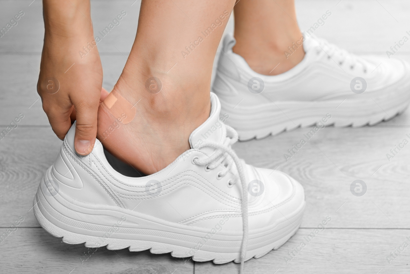 Photo of Woman with plastered heel on wooden floor, closeup view