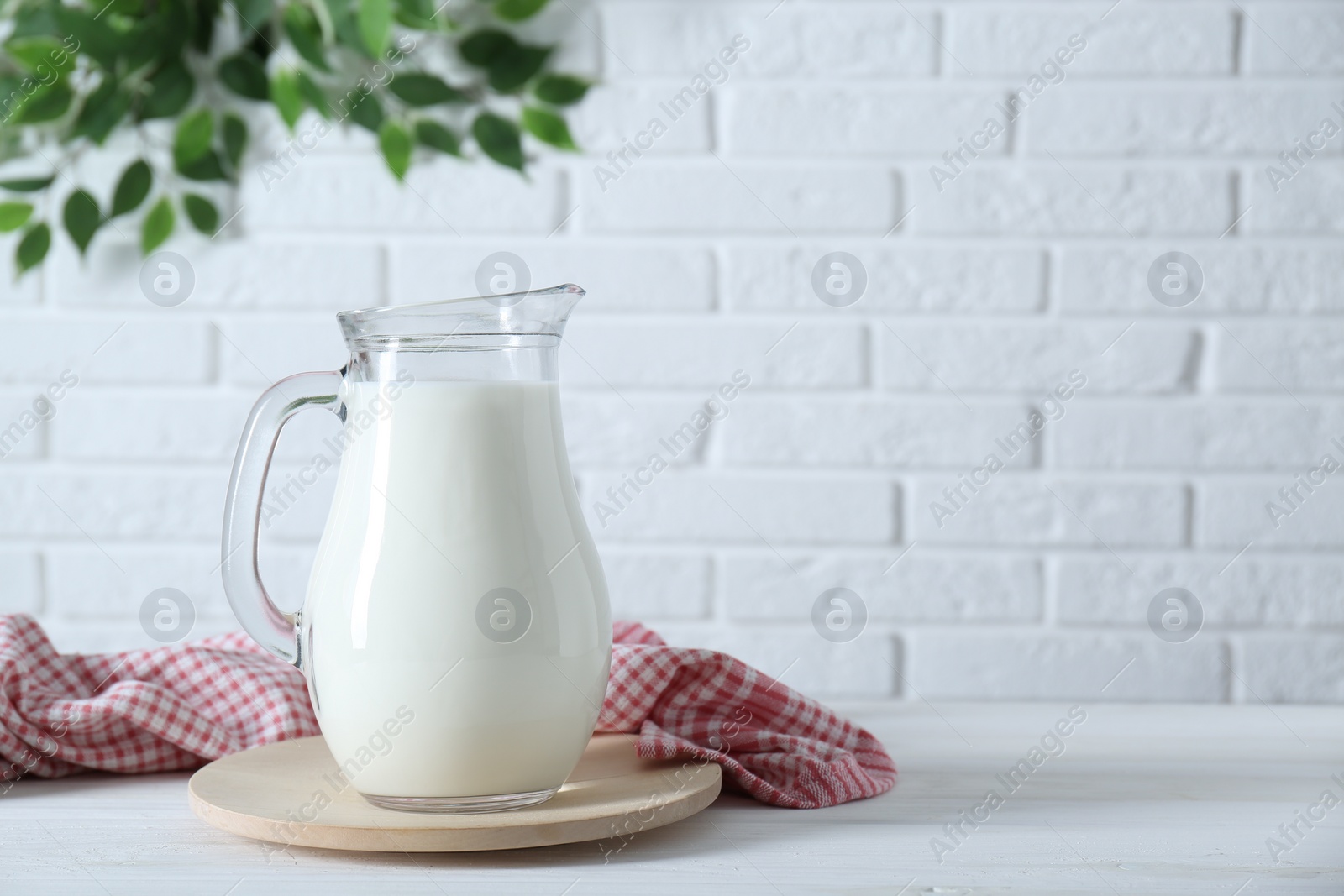 Photo of Jug of fresh milk on white wooden table, space for text