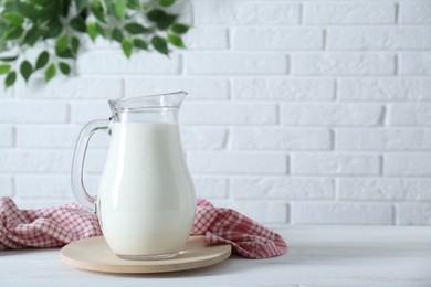 Jug of fresh milk on white wooden table, space for text