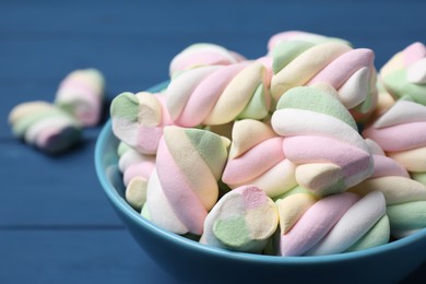 Photo of Bowl with colorful marshmallows on blue table, closeup