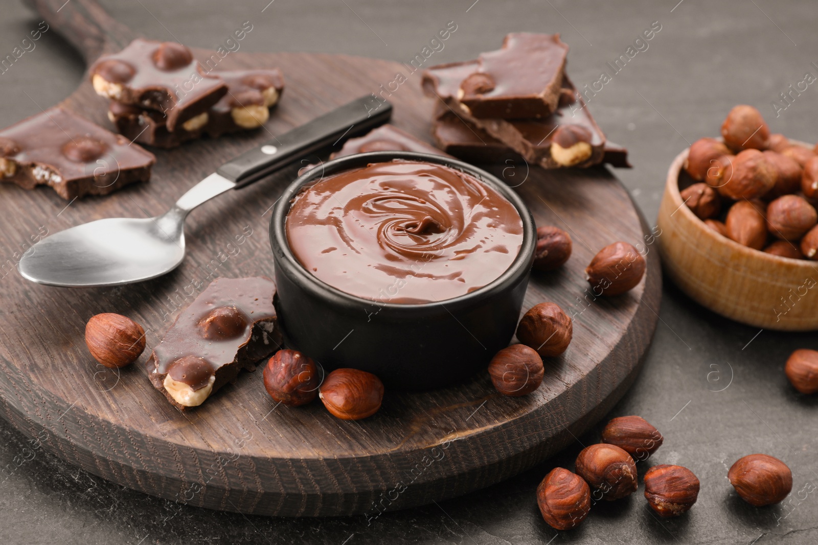 Photo of Bowl with tasty paste, chocolate pieces and nuts on grey table