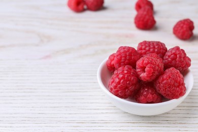 Tasty ripe raspberries in bowl on white wooden table, space for text