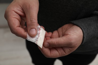 Drug addiction. Man with plastic bag of cocaine on light background, closeup