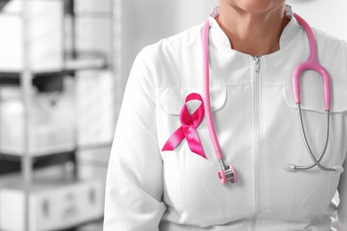 Photo of Doctor with stethoscope and pink ribbon indoors, closeup and space for text. Breast cancer awareness