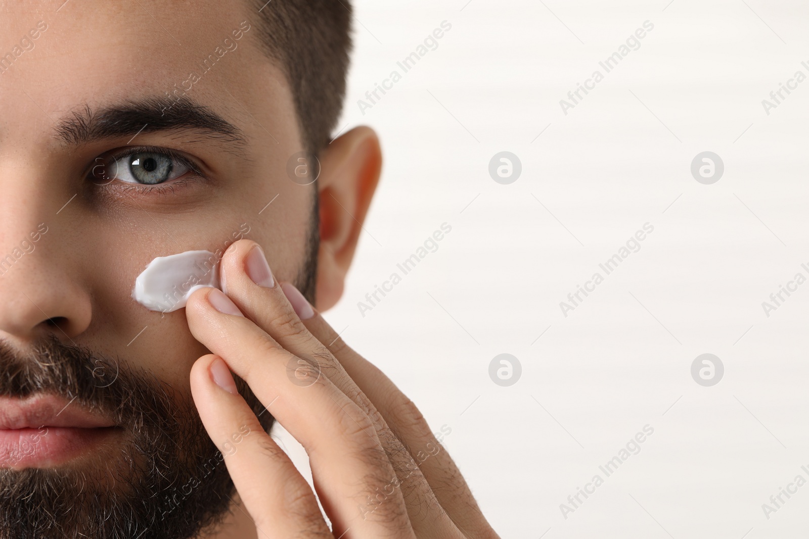 Photo of Man with dry skin applying cream onto his face on light background, closeup. Space for text