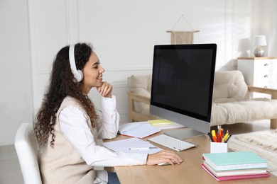 African American woman with headphones using modern computer for studying at home. Distance learning