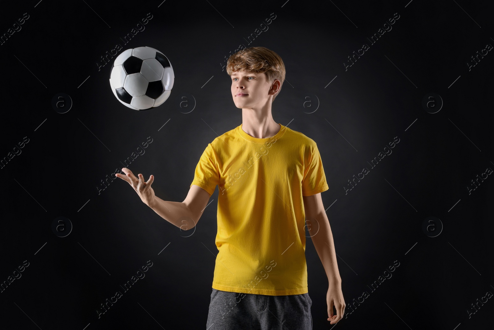 Photo of Teenage boy playing with soccer ball on black background