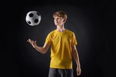 Teenage boy playing with soccer ball on black background