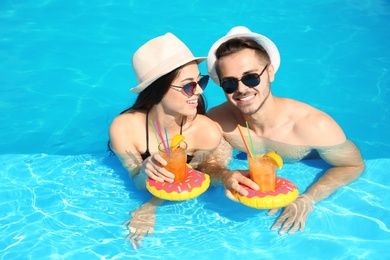 Young couple with refreshing cocktails in swimming pool on sunny day