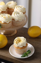 Delicious lemon cupcakes with white cream, mint and lemons on wooden table, closeup