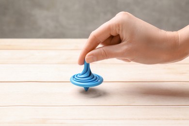Photo of Woman playing with blue spinning top at light wooden table, closeup