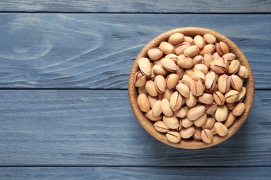 Photo of Organic pistachio nuts in bowl on wooden table, top view. Space for text