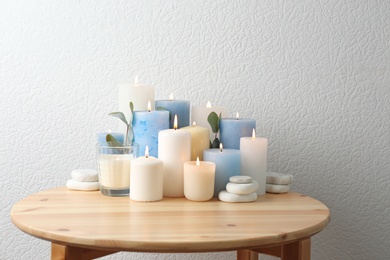 Composition with burning candles on table near white wall