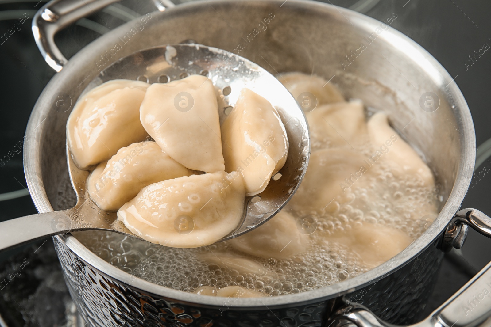 Photo of Closeup of dumplings on skimmer over stewpan with boiling water. Home cooking