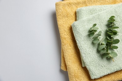 Photo of Soft folded towels with eucalyptus branches on light grey background, top view. Space for text