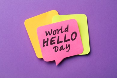 Paper note with phrase World Hello Day on purple background, top view