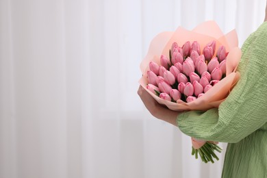 Photo of Woman holding bouquet of pink tulips indoors, closeup. Space for text