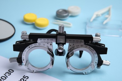 Trial frame with different ophthalmologist tools on light blue background, closeup