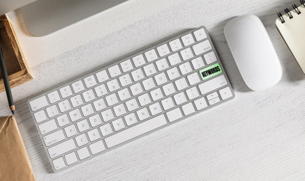 Keyboard with text KEYWORDS on white wooden table, flat lay