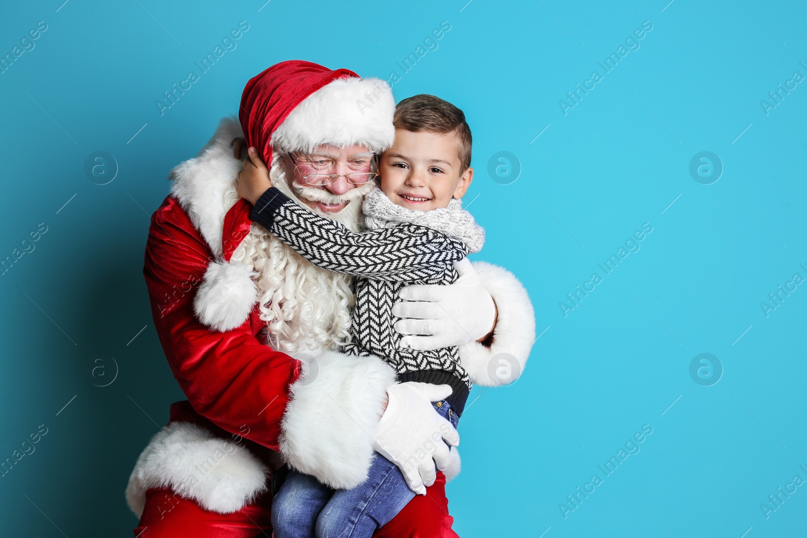 Photo of Little boy hugging authentic Santa Claus on color background