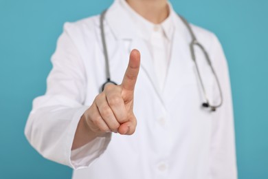 Doctor with stethoscope pointing on light blue background, closeup